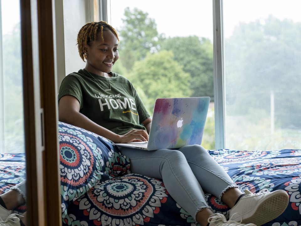 A student in her room, sitting on her bed looking at her laptop