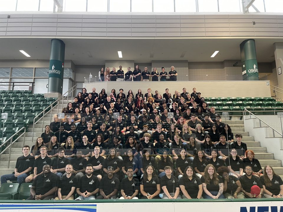 Residence Life and Housing staff sitting on the stands of the ice arena, wearing Res Life polos. 