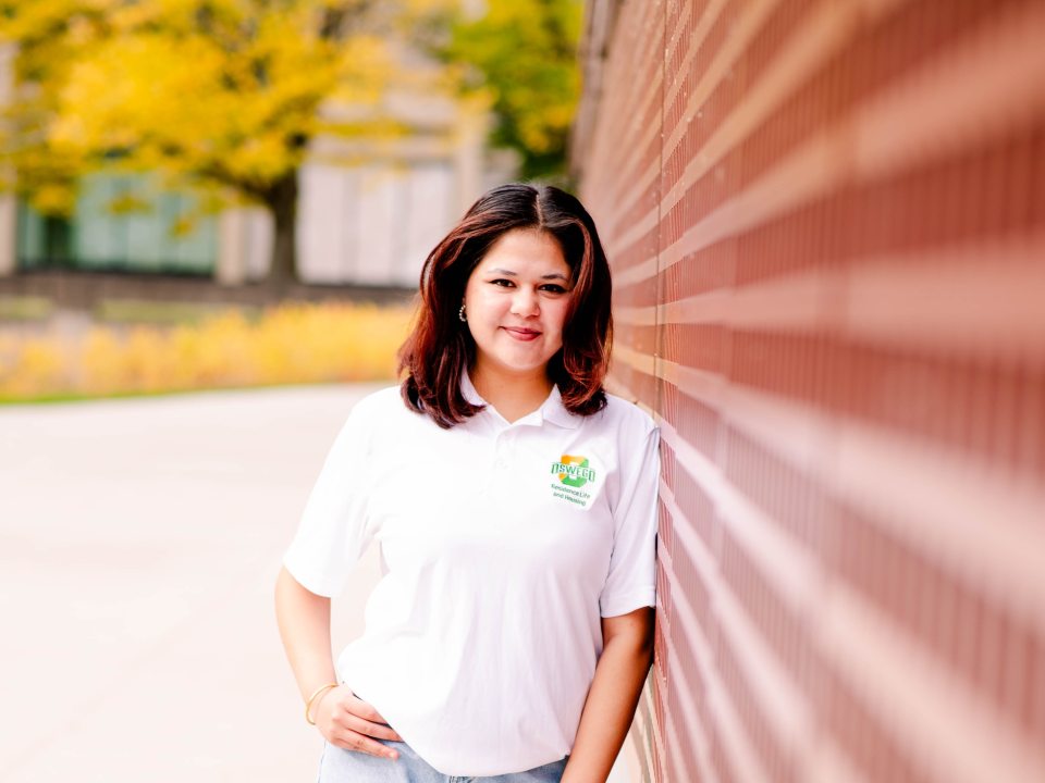 RA in a polo leaning on a brick wall 