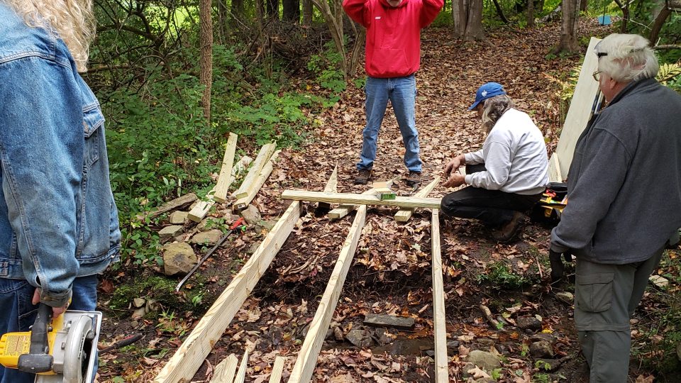 Four people stand in a trail building a boardwalk