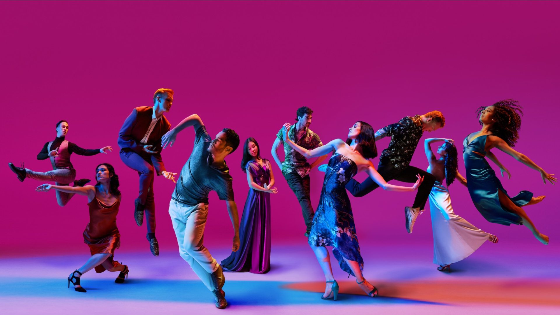 A group of dancers in blue costumes performing on a stage lit in pink