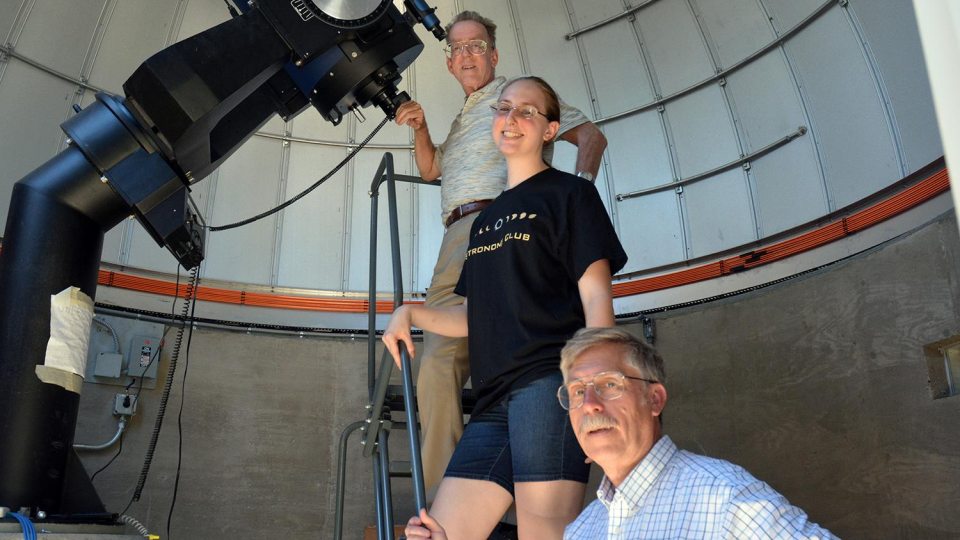Three people standing in an observatory with a telescope