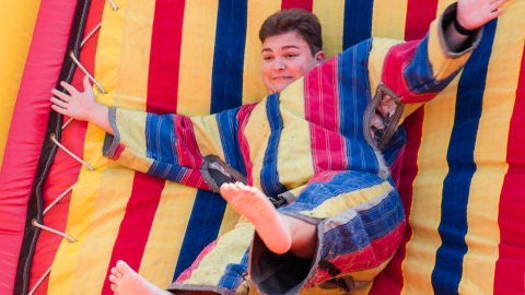 A student in a brightly colored striped velcro suit stuck to a velcro wall