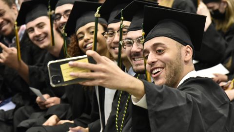 Excited graduates in caps and gowns snap a group selfie at commencement.