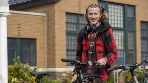 A student smiles for a quick photo while parking his bike in front of Riggs Hall.