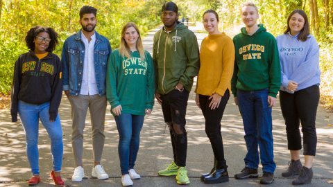 Seven Oswego students smile on a fall path.