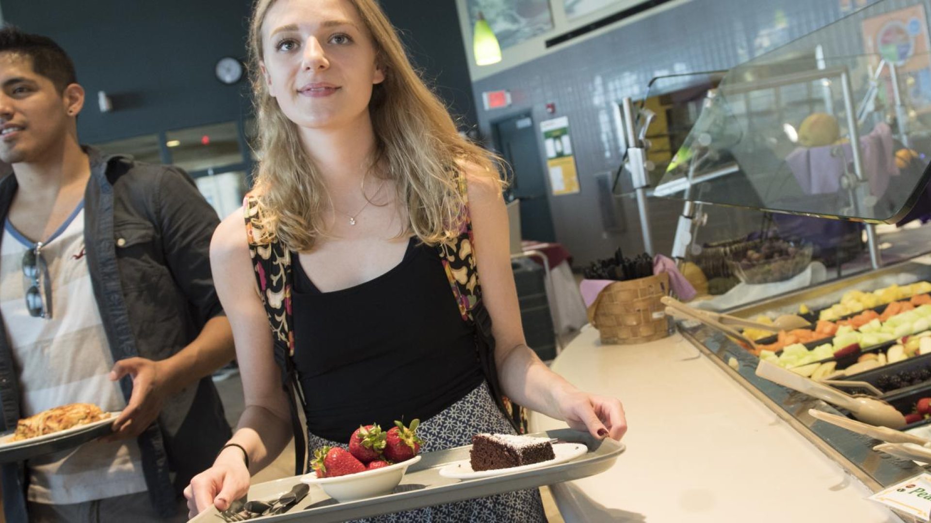 Two students carrying trays in a dining gall