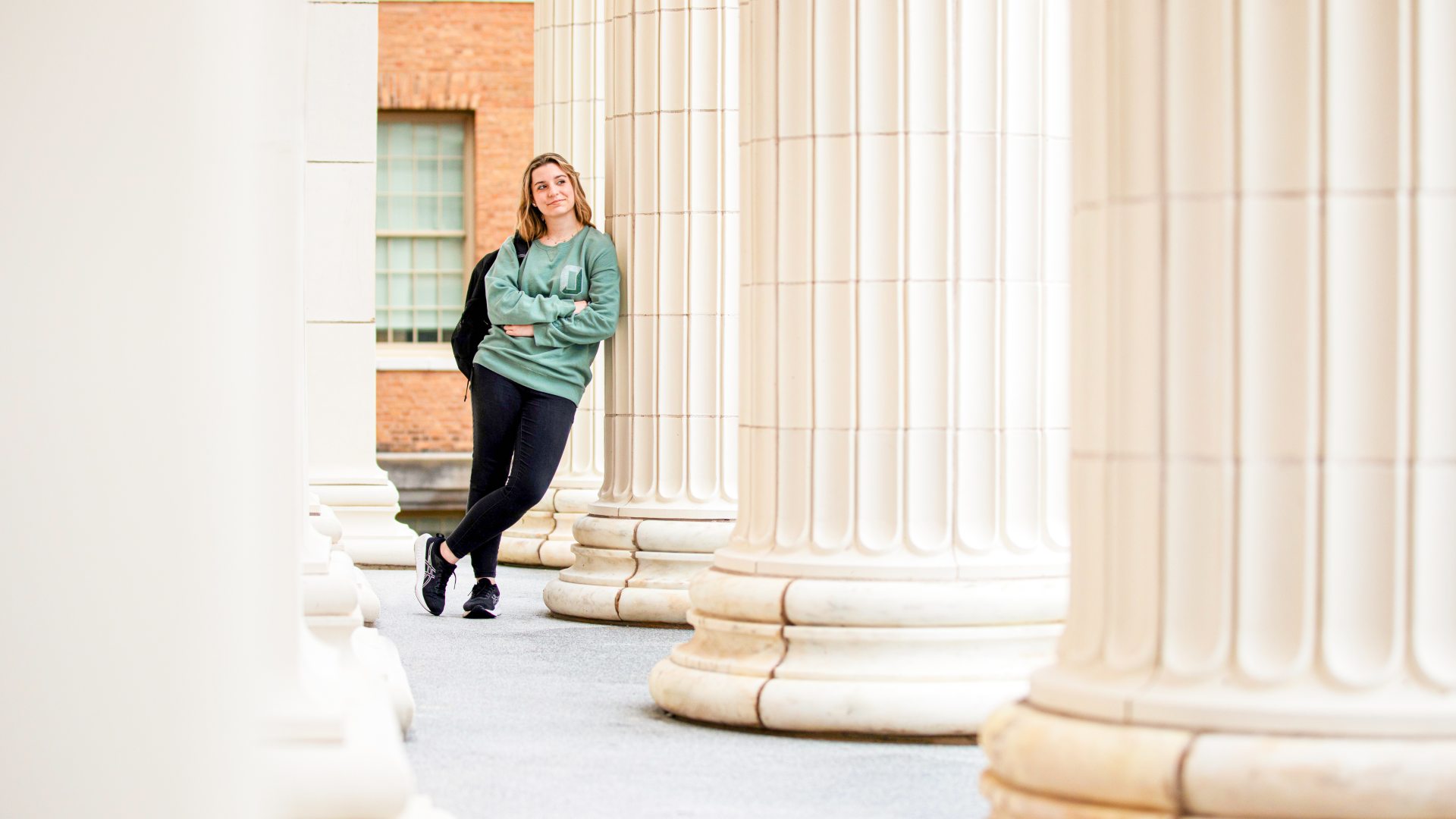 A young woman leans on the columns of historic sheldon hall.