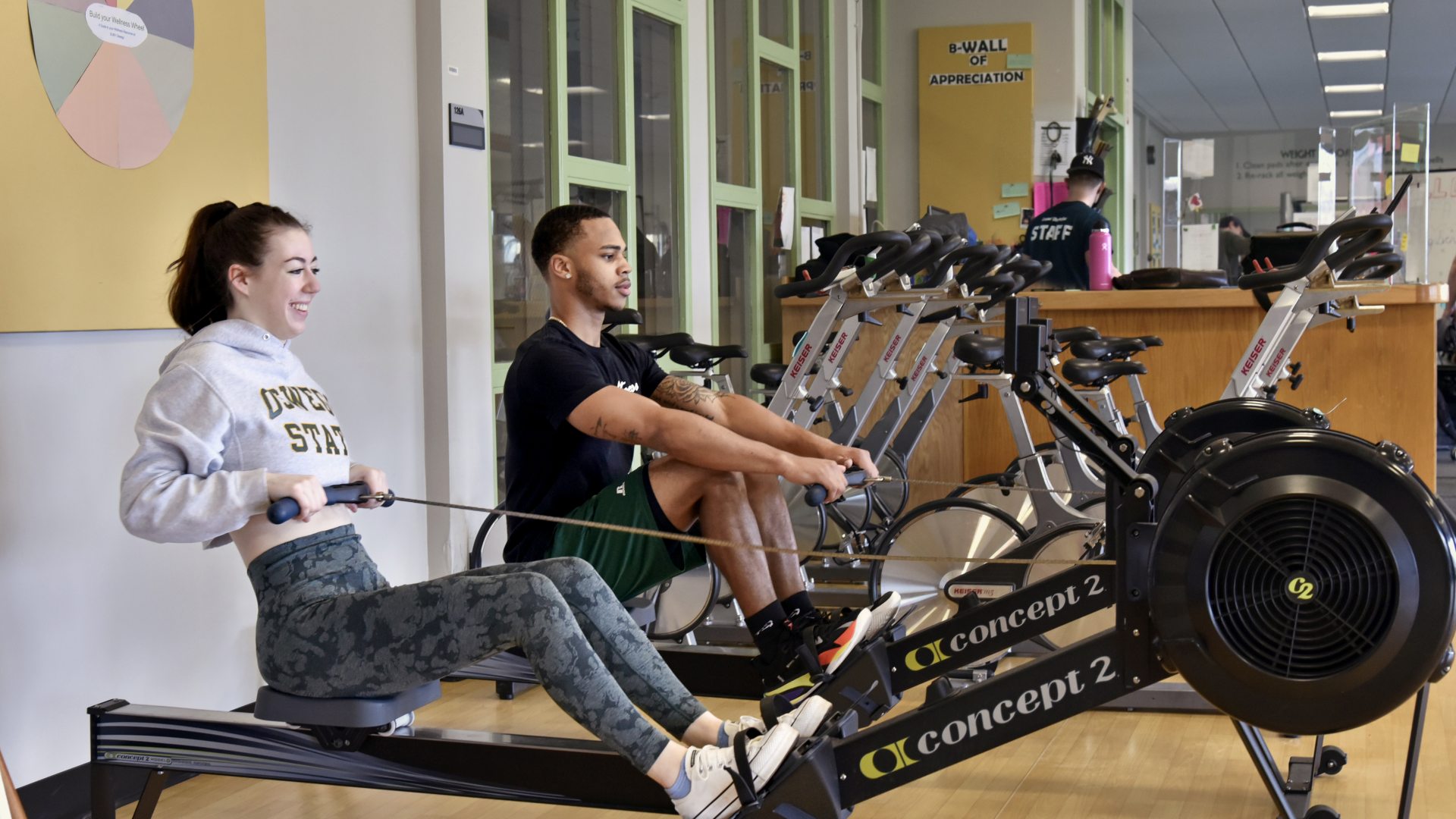 Two students working out on rowing machines in a fitness center.