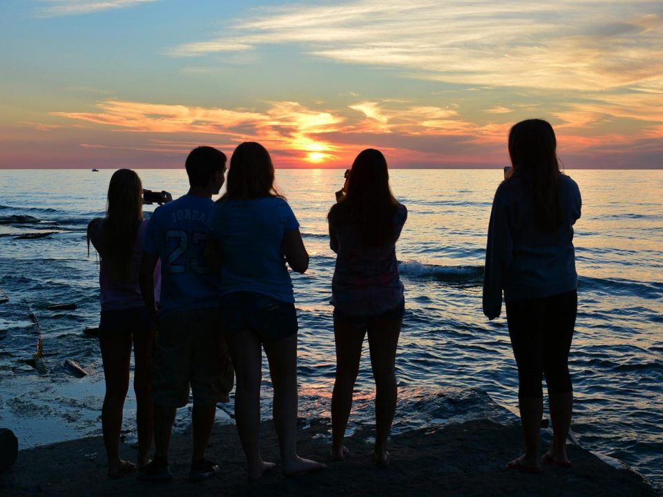 Students looking at and taking photos of a sunset over Lake Ontario