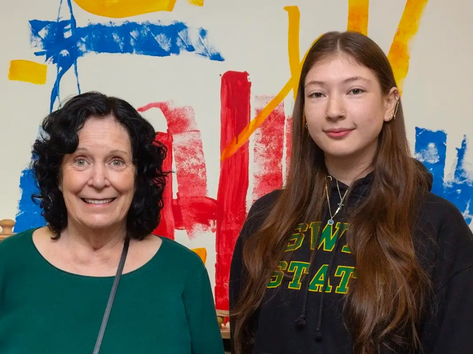 Sarah-Michelle Soto standing with another person in front of a colorful mural at the Oswego Children&#039;s Center.