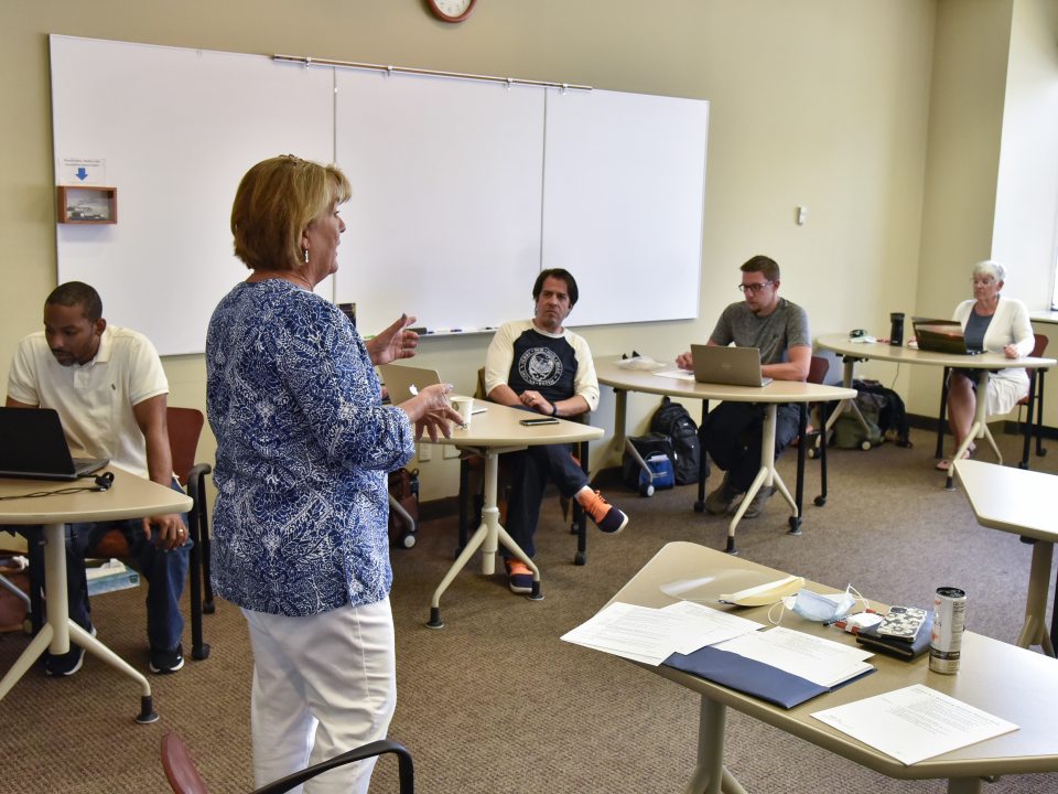 An instructor leads a discussion with adult learners seated around a classroom, participating in a small-group learning environment at SUNY Oswego at Syracuse.