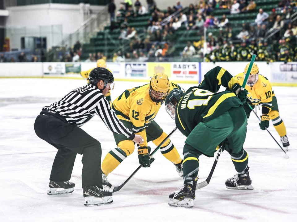SUNY Oswego hockey players face off on the ice as a referee prepares to drop the puck.