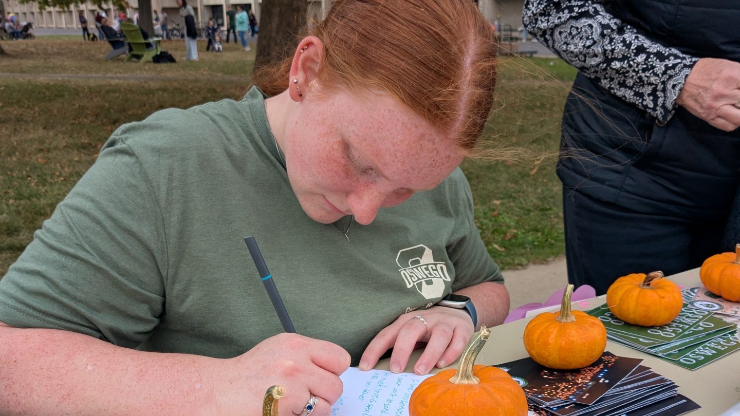 Student filling out a postcard surrounded by fall decor
