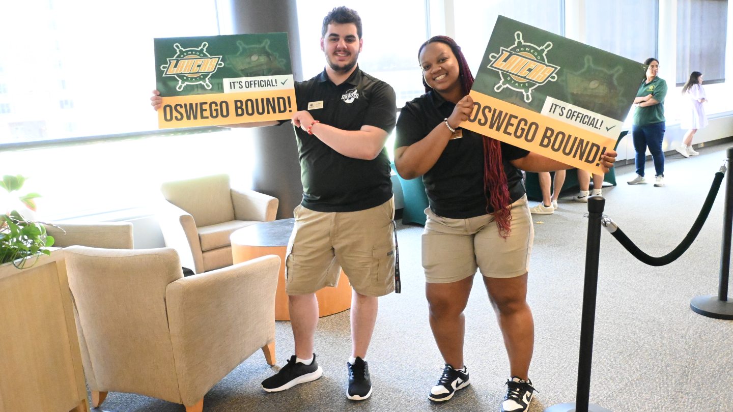 Two Orientation Leaders holding "Oswego Bound!" signs smiling into the camera