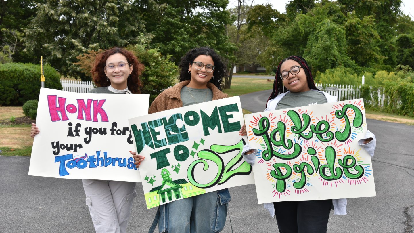 Res Life student staff members holding funy signs to welcome students as they drive into campus