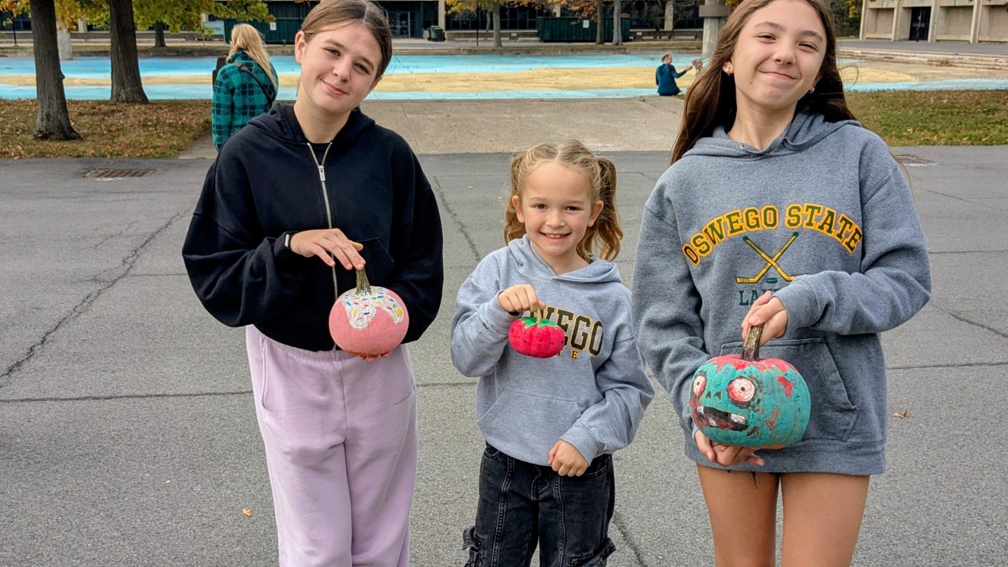 A student with younger siblings holding pumpkins they painted.