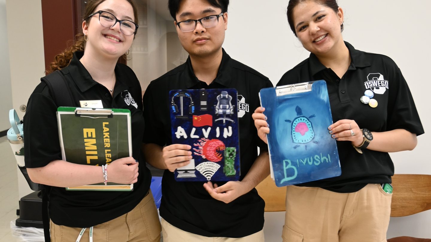 Three Orientation Leaders showing off their decorated clipboards and smiling into the camera.