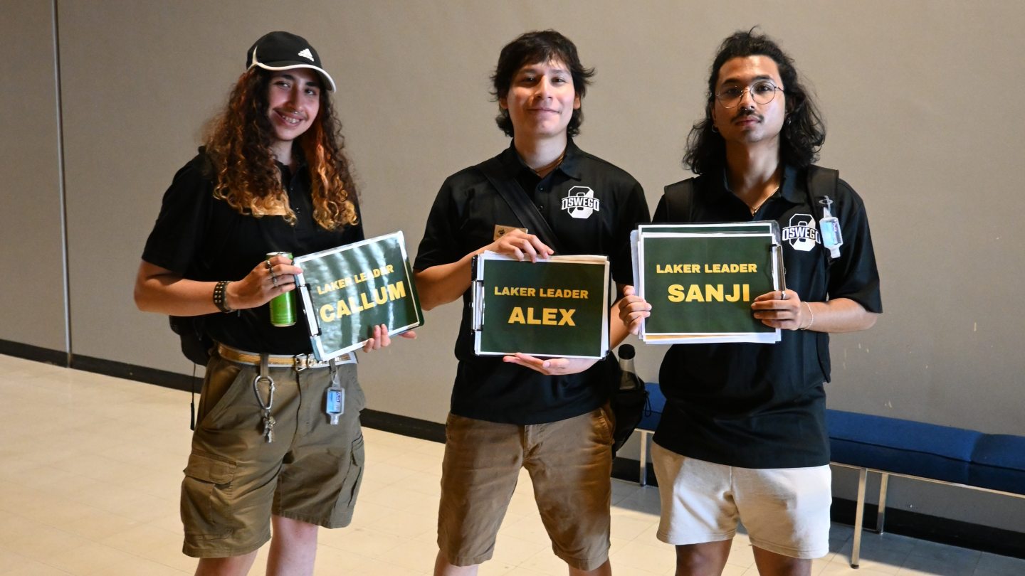 Three Orientation leaders holding signs with their names, smiling toward the camera