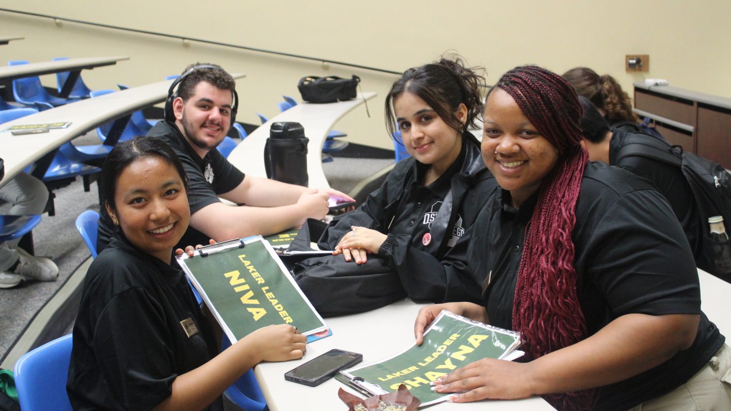 Four Orientation Leaders organizing papers and smiling into the camera