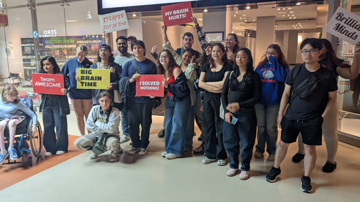 Orientation Leaders standing outside an escape room with signs celebrating their win!