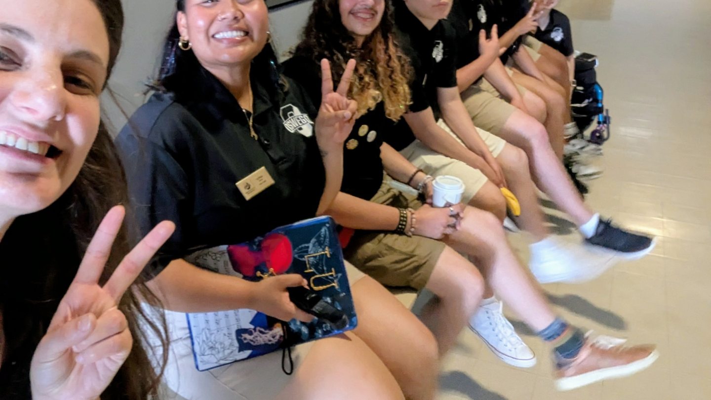 Orientation leaders sitting on a table, smiling and swinging their feet.