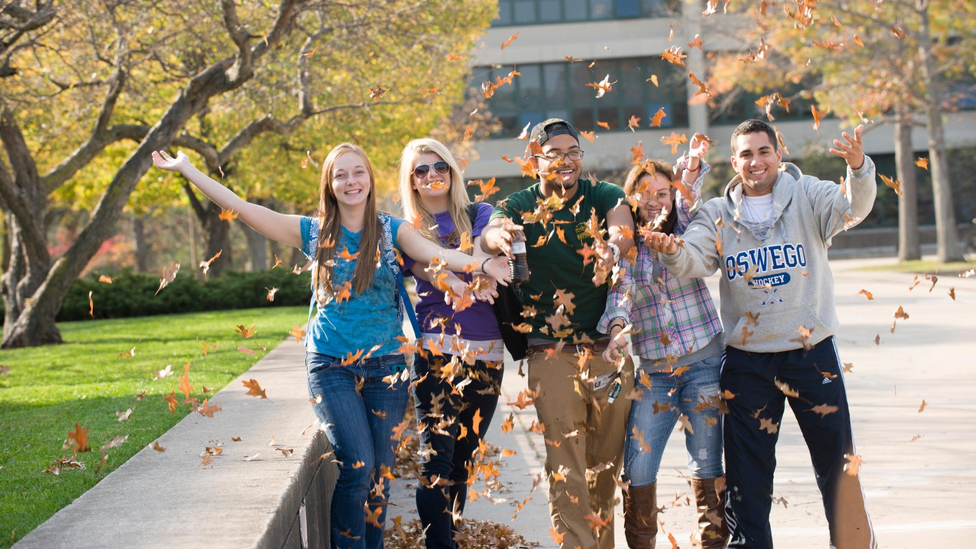 A group of students outside, throwing leaves into the air