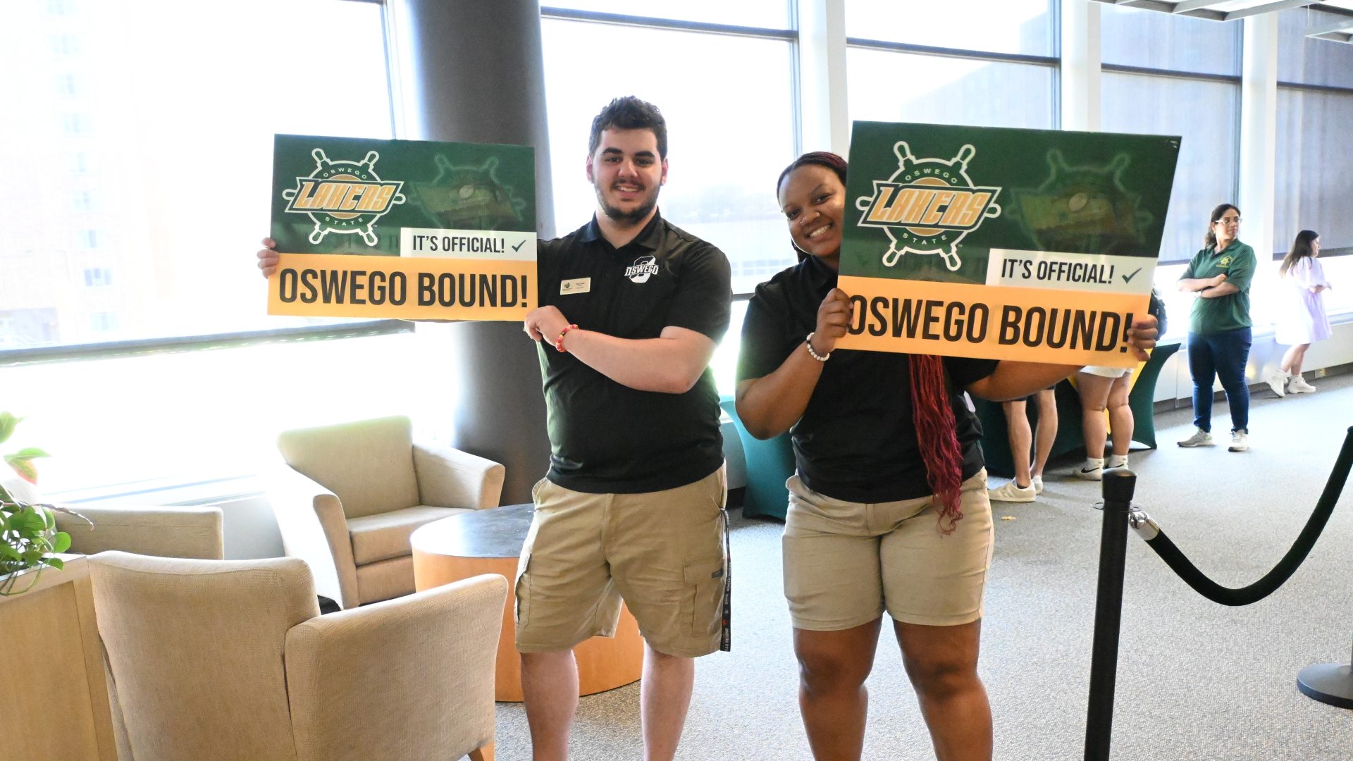 Two Orientation Leaders holding "Oswego Bound!" yard signs smiling at the camera
