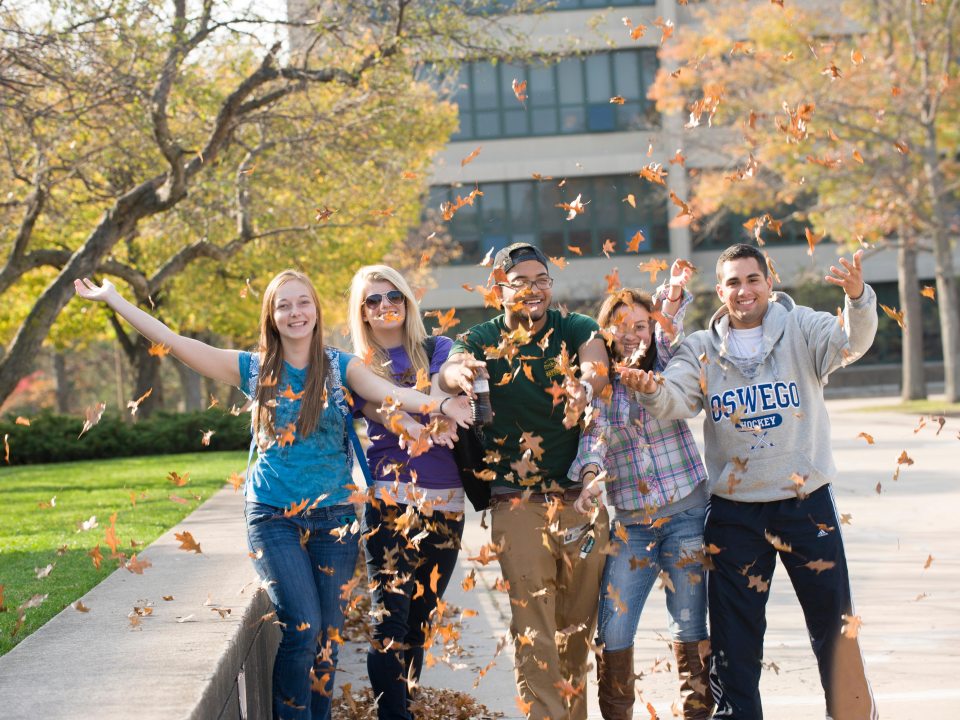 A group of students outside, throwing leaves into the air