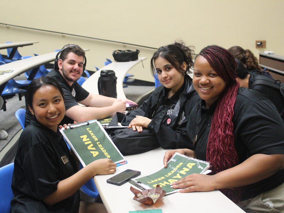 Four Orientation Leaders organizing papers and smiling into the camera