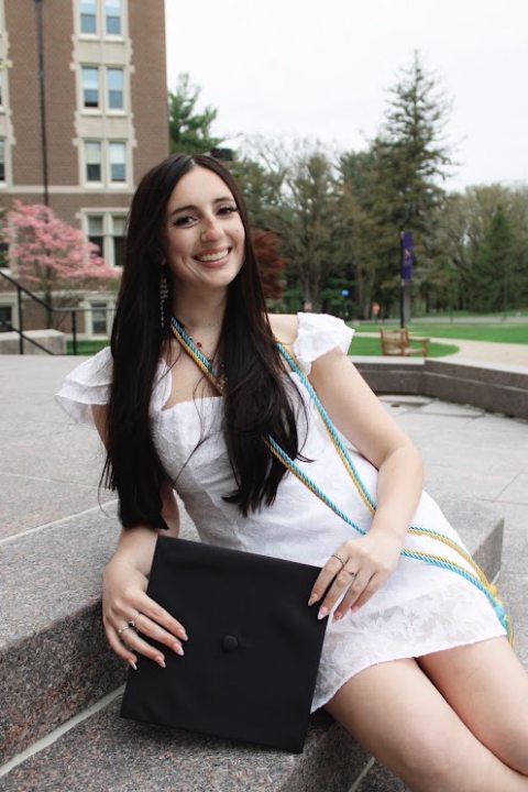 A photo of Bri in her graduation gown, wearing her cords and holding her undergraduate degree.