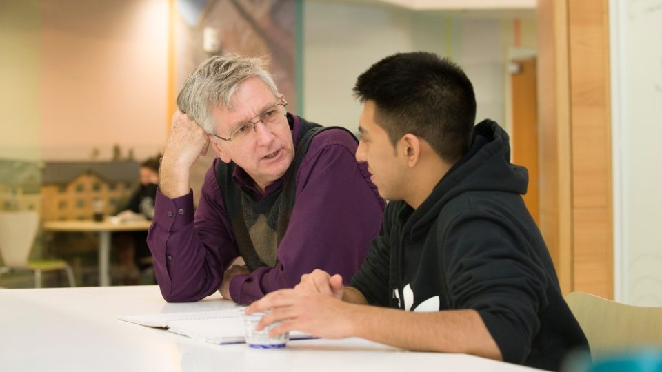 A student and professor talking together at a table