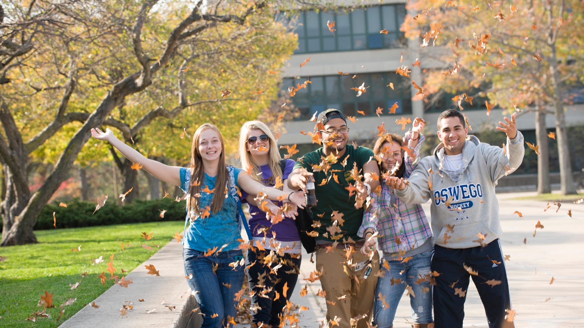 Students standing outside, throwing leaves into the air
