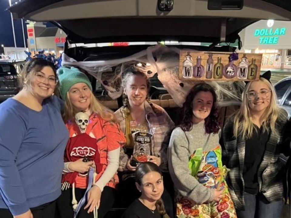 Members of Kappa Delta Phi posing next to a car decorated for Trunk or Treat