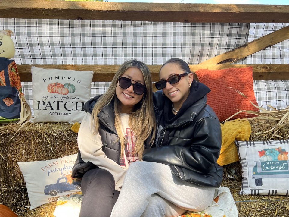 Two female students smiling, sitting on a bale of hay at Pumpkinfest