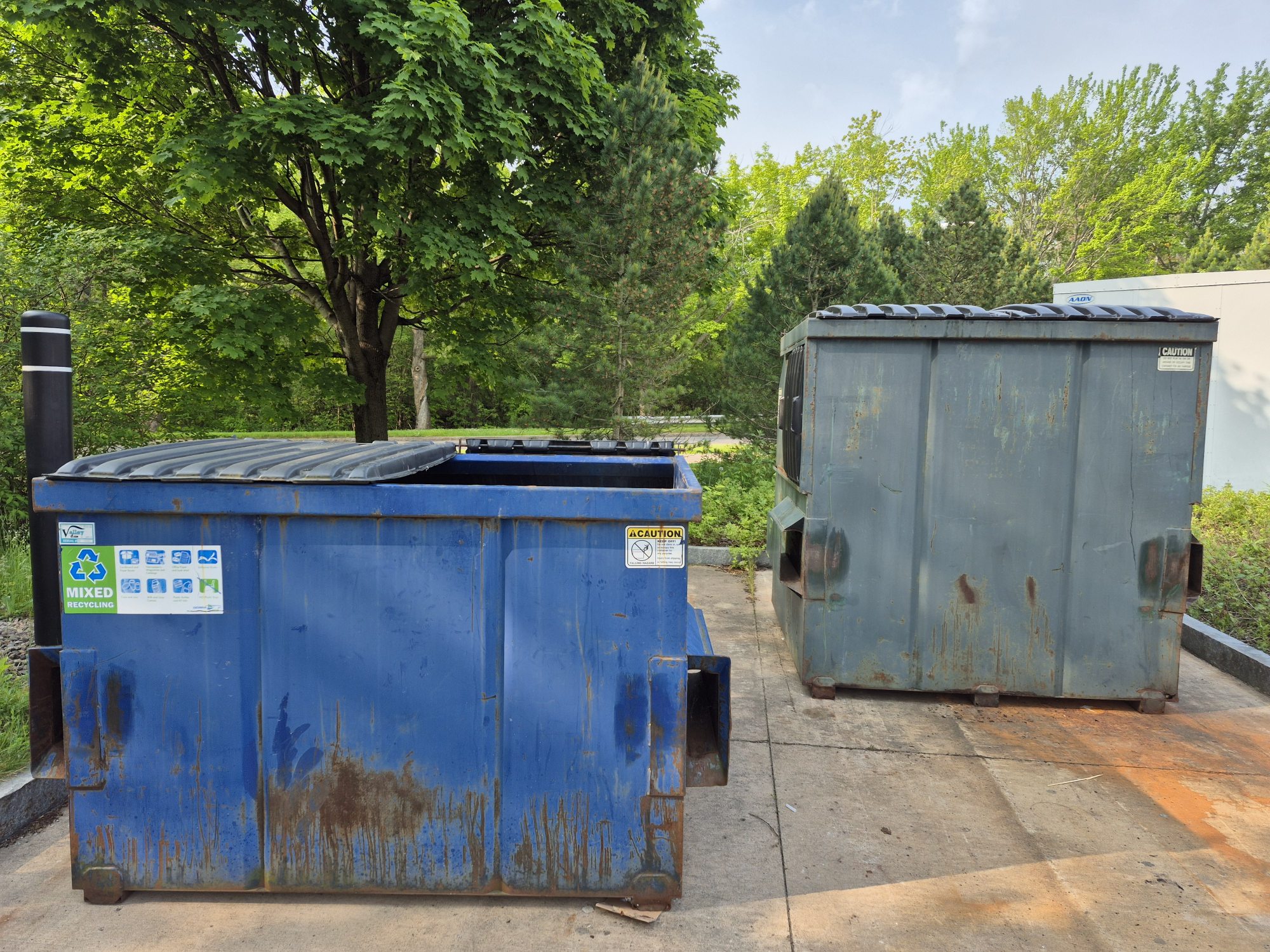 Blue recycling dumpster and Green Trash dumpster in village parking lot