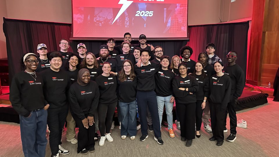 TEDx SUNY Oswego team wearing their hoodies in front of the stage.