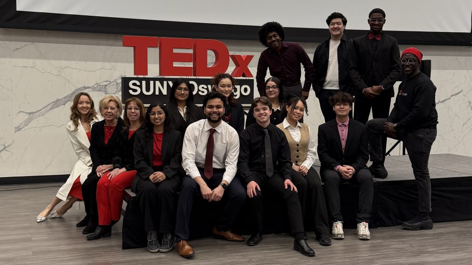 Photo of the TEDx team on the stage with the sing in the background