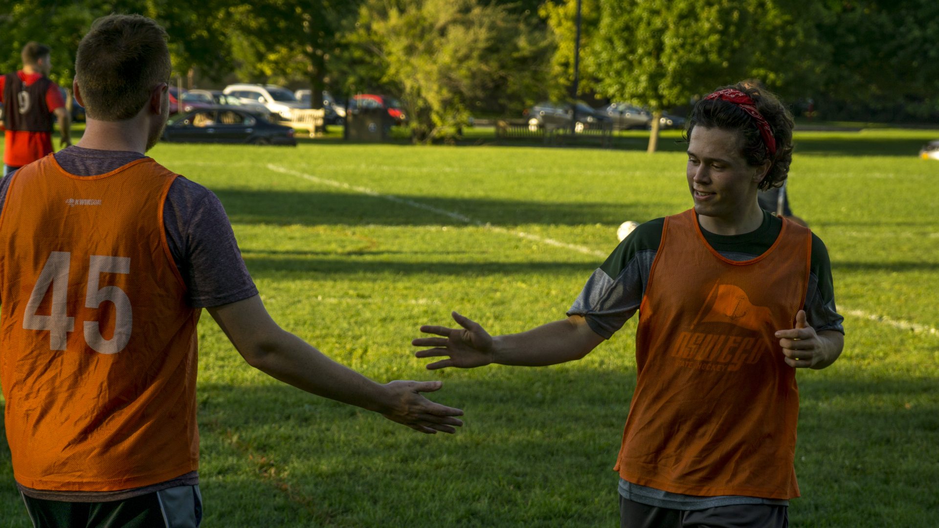 Two people wearing orange jerseys on a playing field, slapping hands as they pass each other 