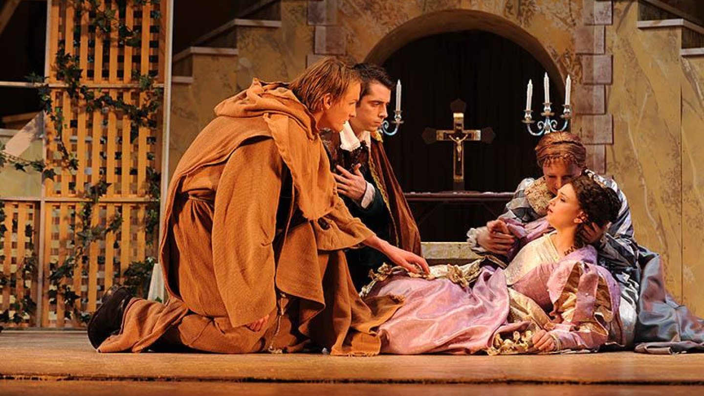Two actors kneeled before an actress lying on the ground on stage. Another actor behind the woman holding her head gently