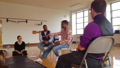 group of students sitting in a practice area talking and making hand gestures