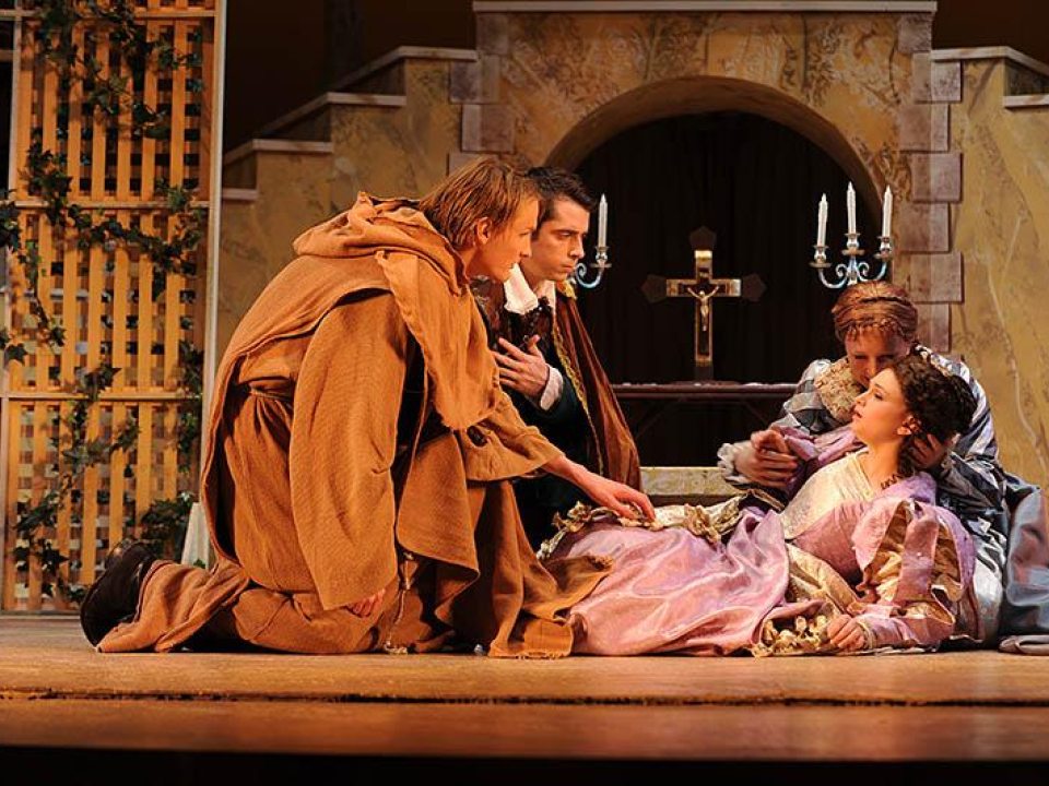 Two actors kneeled before an actress lying on the ground on stage. Another actor behind the woman holding her head gently