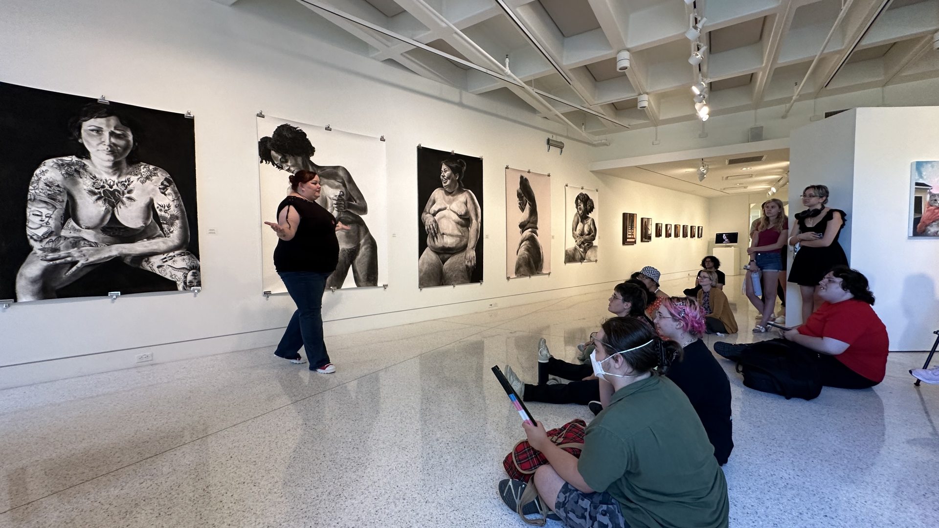 Lindsey Guile talks to student about her large scale figurative drawings which are displayed behind her