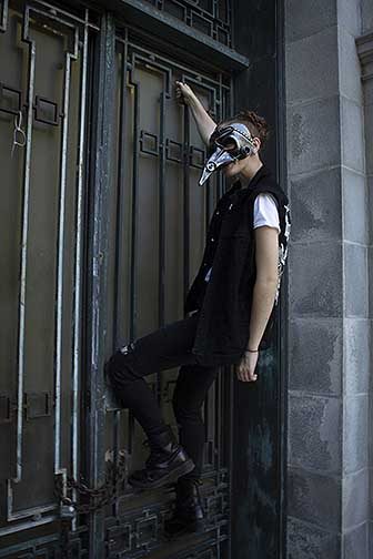 Photograph of a young girl with a steampunk plague mask hanging off a tomb.