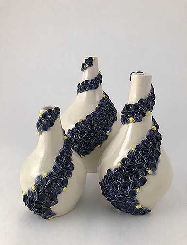 This is a set of three vases( One large, one medium and one small) which are made from porcelain clay. These pieces have blue small finger pressed designs added to the surface flowing up to the opening of the vase. Bright yellow pistils were randomly added around these pieces as well.