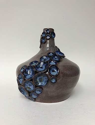 This piece is a smaller thrown piece made from red clay. Larger thumb print details were added to this vase. This vase was glazed in clear and then on the details artic blue glaze was added.