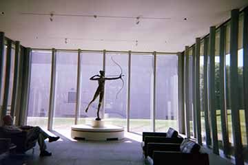 A photograph of a lobby with a man sitting in a chair and a statue holding a bow and arrow.