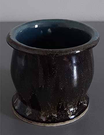 An imperfect mug somewhat lopsided with a pale blue interior glaze and a dark brown exterior glaze with a metallic sheen.