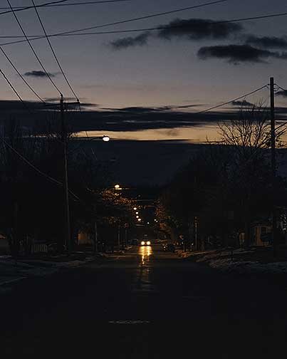 A dark street with cars headlights in the distance.