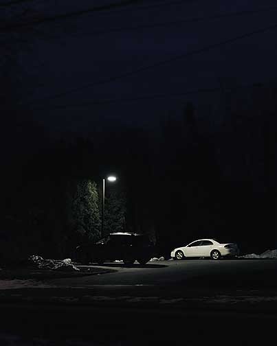 A parking lot light illuminating a white car.